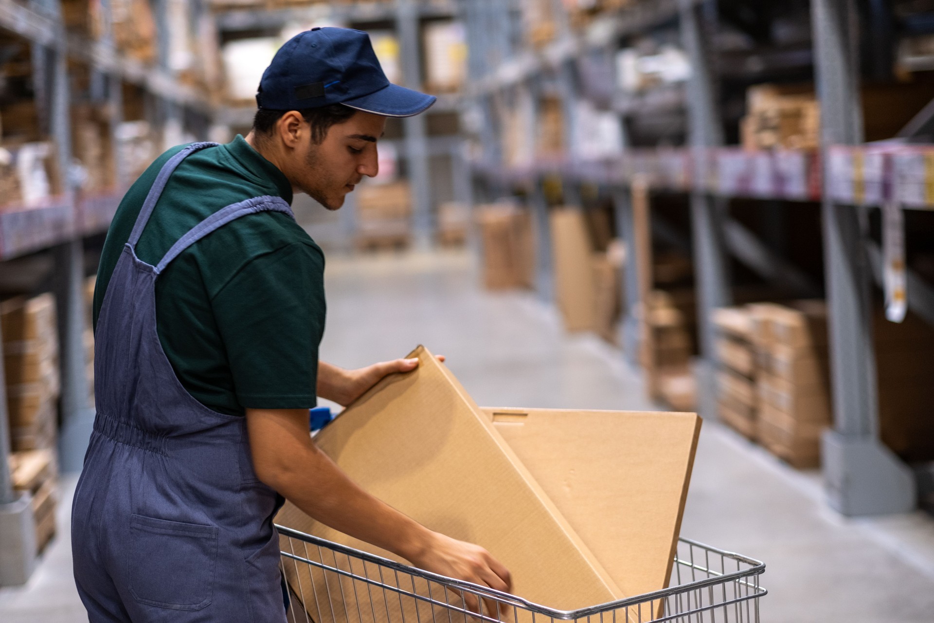 Young warehouse worker arranging furniture panels in a shopping cart inside a warehouse, preparing an order for delivery